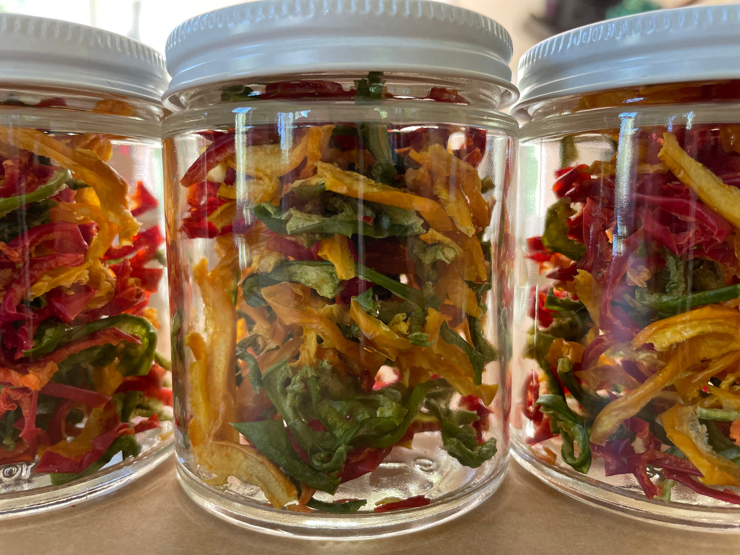 Three clear glass jars of dried multicolored bell peppers