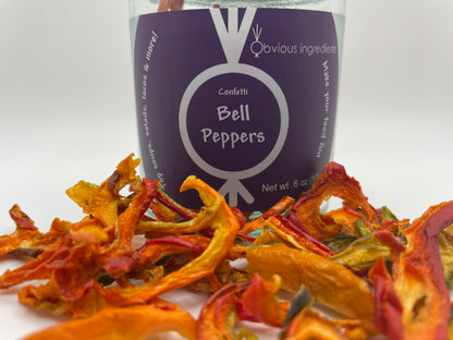 Clear jar of dried bell peppers with purple label surrounded by sliced dehydrated bell peppers