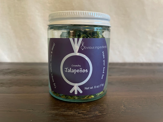 Jar of dried jalapeños on a wood table with a light-colored background