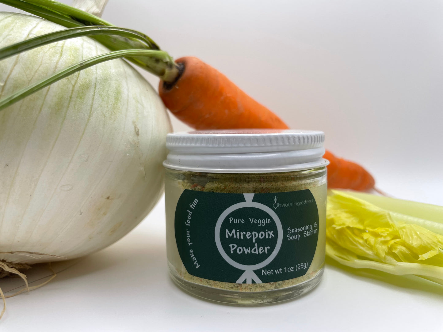 Jar of mirepoix powder surrounded by whole onion, carrot and celery stock with white background