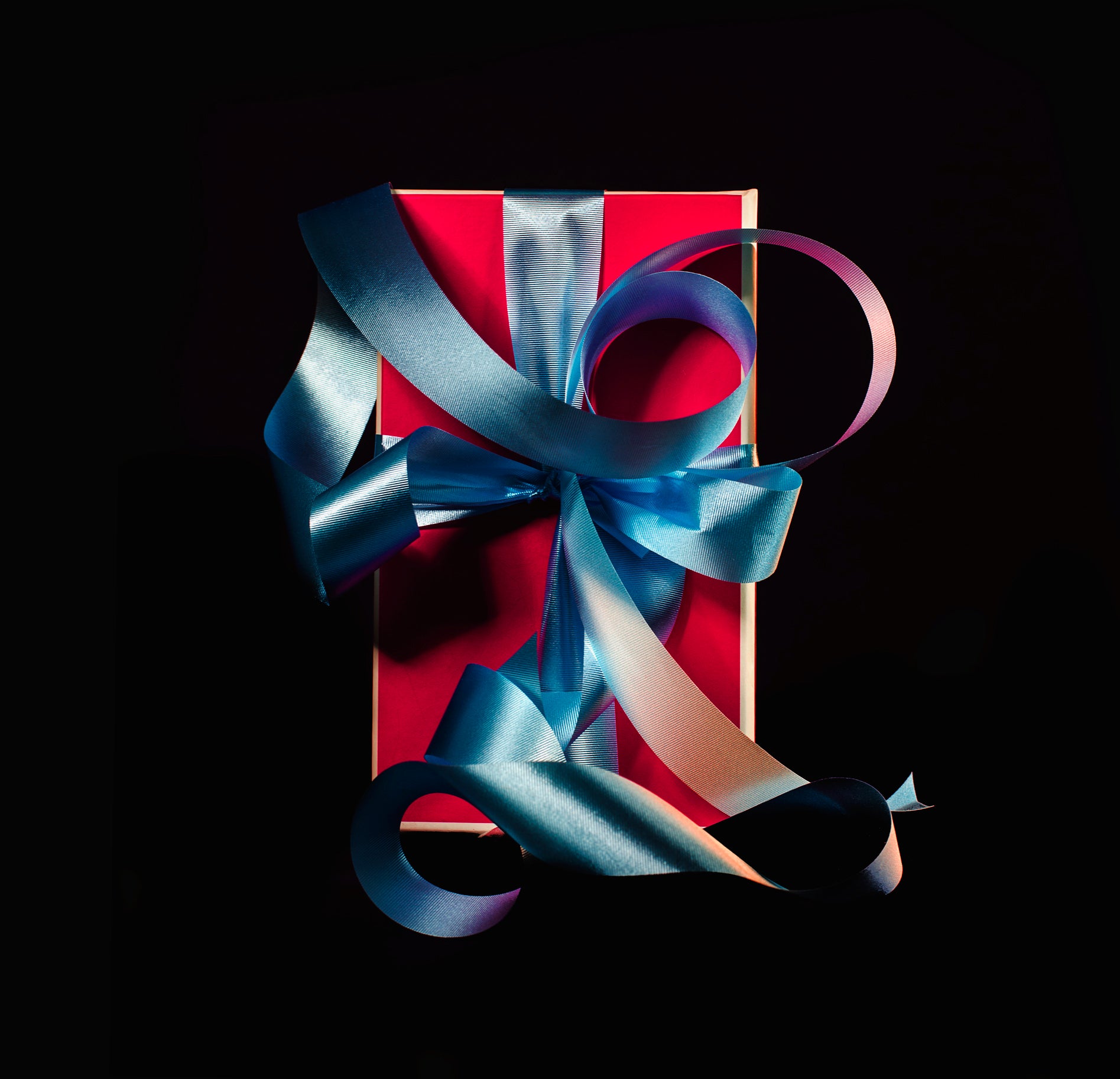 Red gift package tied with fancy blue ribbon on a black background